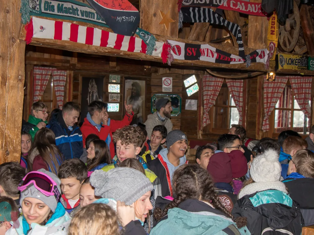 Volle Hütte mit geschmückter Decke und vielen Gästen.